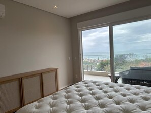Ein Schlafzimmer mit einem großen Bett, Meerblick und einem Balkon mit Gartenmöbeln.