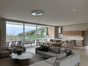 Ein modernes Wohnzimmer mit Sofa, Couchtisch und Sesseln, ein Balkon mit Essbereich und eine Küche mit Holzausstattung.
