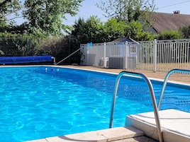 Una piscina azul cristalina con una escalera metálica y un área cercada.