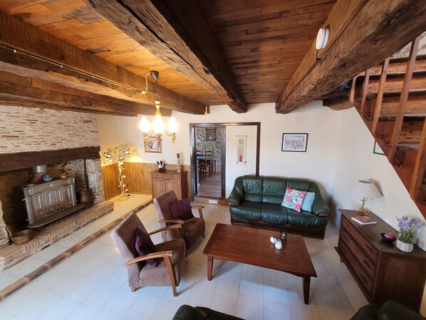 A rustic interior with a fireplace, wooden beams, a green sofa, and a dining area. - Authentic Gite With Terrace and Shared Pool (Saint-Saud-Lacoussiere)