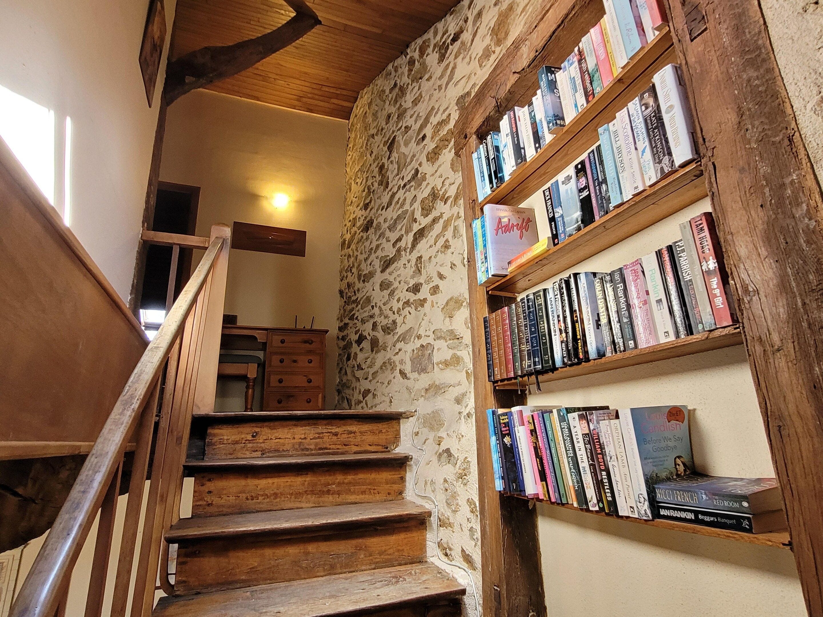A staircase leading to a room with a stone wall and wooden bookshelves filled with books.