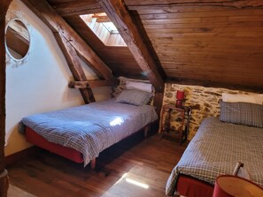 A small, rustic room with two beds, wooden beams, a stone wall, and a skylight. - Authentic Gite With Terrace and Shared Pool (Saint-Saud-Lacoussiere)