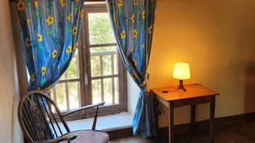 A room with a wooden floor, a chair, a table with a lamp, and a window with curtains.
