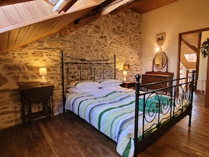Un dormitorio con pared de piedra, una cama con colcha a rayas, dos lámparas de noche y una mesita de noche de madera.