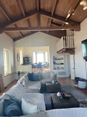 A spacious living room with a high wooden ceiling, a large sectional sofa, a coffee table, and a dining area in the background. - Fabulous 3-bedroom house in Laguna Beach with breathtaking panoramic ocean views (Laguna Beach)