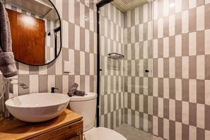 Une salle de bain avec un mur recouvert de carreaux à motifs à carreaux, un lavabo rond, des toilettes et un espace douche.