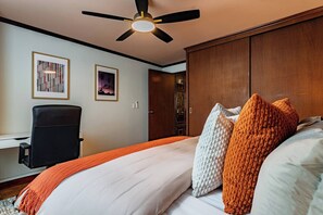 Une chambre à coucher comprenant un lit, des oreillers, un bureau, une chaise, un ventilateur de plafond et une armoire.