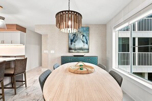 A dining area with a round table, chairs, a hanging light fixture, a painting, and a window with a view. - Captiva Hide-A-Way 1B (Captiva)