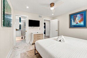 A hotel room with a bed, a television, a ceiling fan, and a painting on the wall. - Captiva Hide-A-Way 1B (Captiva)