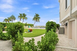 A landscaped outdoor area with palm trees, a well-maintained lawn, and a building with a beige exterior. - Captiva Hide-A-Way 1B (Captiva)