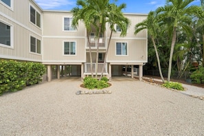 A multi-story building with a covered outdoor area, palm trees, and a gravel driveway. - Captiva Hide-A-Way 1B (Captiva)