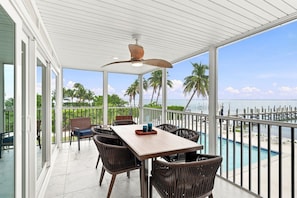 A covered outdoor area with a table and chairs, a ceiling fan, and a view of the beach and ocean. - Captiva Hide-A-Way 1B (Captiva)
