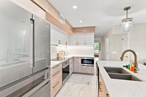 A modern kitchen with stainless steel appliances, wooden cabinets, and a marble countertop. - Captiva Hide-A-Way 1B (Captiva)