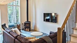 A modern living room with a sectional sofa, a round coffee table, a fireplace, and a mounted TV. - Nordic Forest Chalet near Mont Tremblant | 32+ Days | Pet Friendly! (Lac-Supérieur)