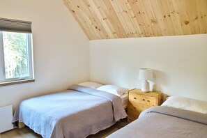 Un dormitorio con dos camas, una mesita de noche con lámpara y una ventana con persianas.