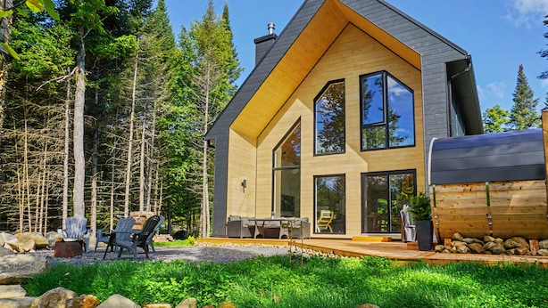 A modern house with a large front porch, a dining area, and a view of the surrounding forest. - Nordic Forest Chalet near Mont Tremblant | 32+ Days | Pet Friendly! (Lac-Supérieur)