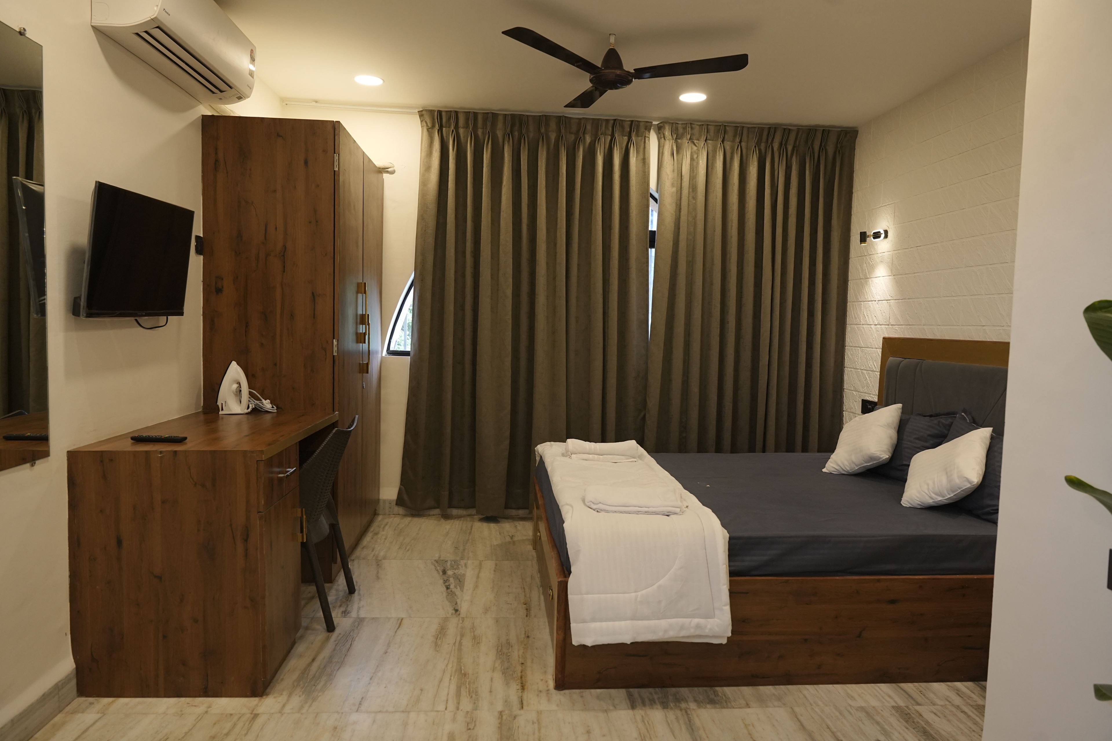 Ein Hotelzimmer mit Bett, Schreibtisch, Fernseher und Deckenventilator.