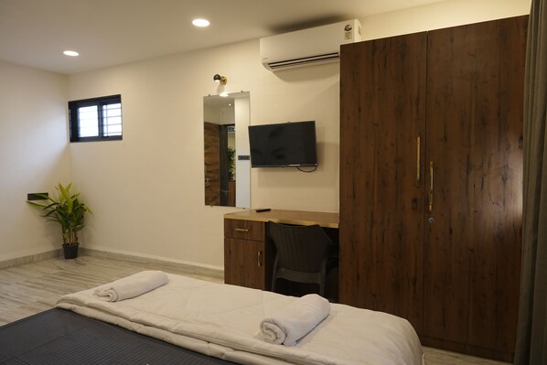 A hotel room with a bed, a desk, a chair, a TV, a wardrobe, and a potted plant.
