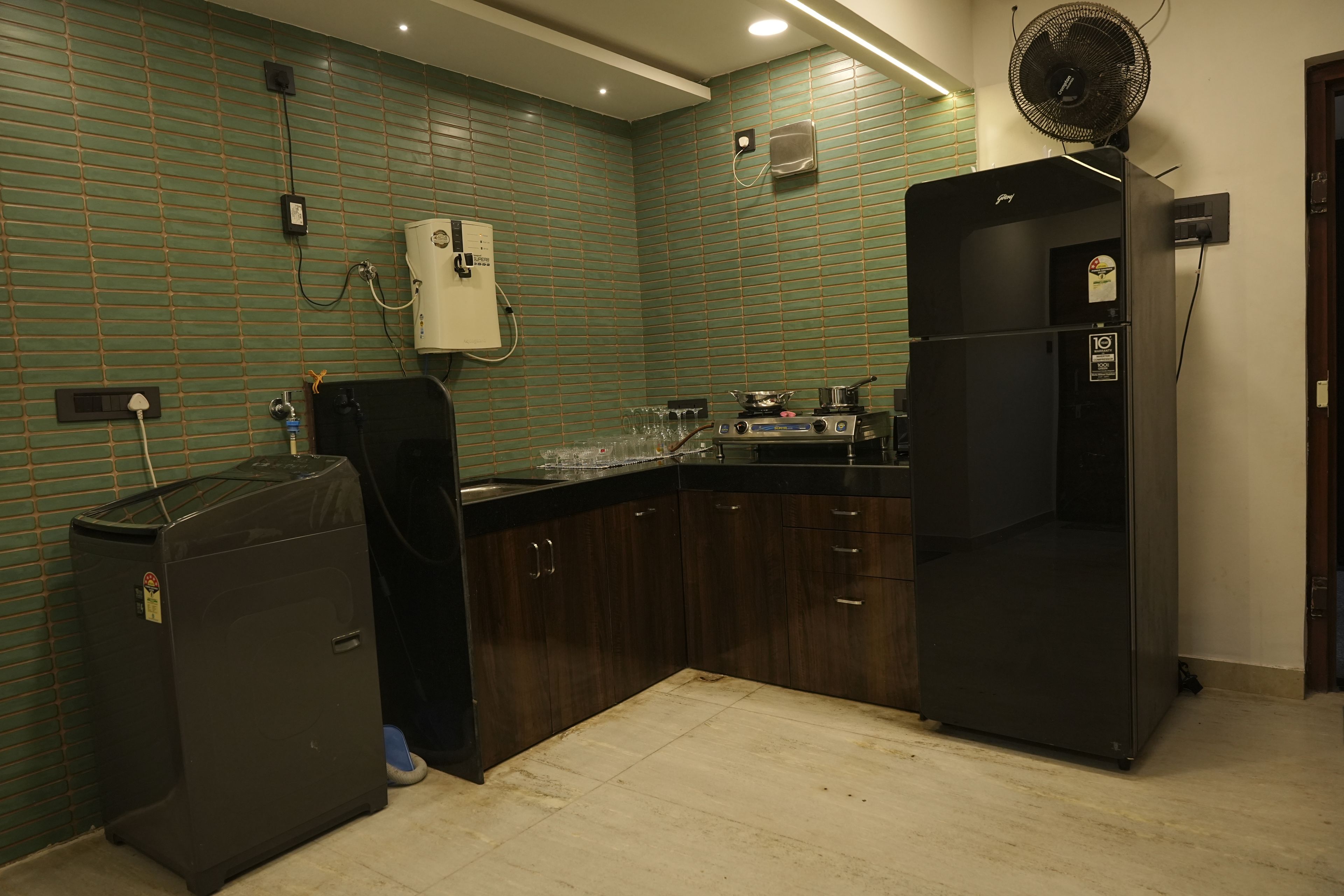 Een keuken met groene betegelde muren, een boiler, een koelkast en een spoelbak.