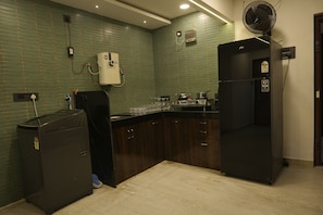 Een keuken met groene betegelde muren, een boiler, een koelkast en een spoelbak.