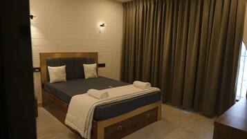 A bedroom with a wooden bed frame, a dark mattress, two pillows, a white blanket, and a wooden nightstand.