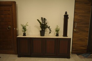 A wooden door with a decorative panel, a marble-top cabinet with potted plants, and a tall, ornate column.