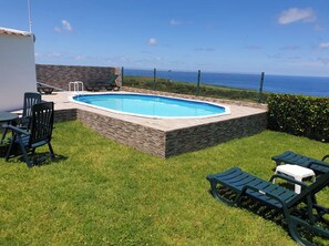 A swimming pool with a stone border, surrounded by grass and a fence. - Rocha Mar House | Country House with Private Pool and Ocean View (Nordestinho)