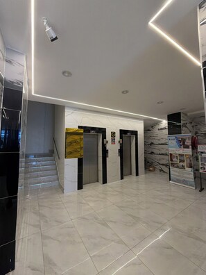 A modern interior with a marble floor, a staircase, and two elevators.