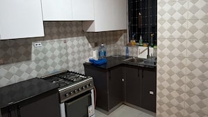 Cocina compacta con estufa a gas, horno y ventana con diseño de celosía.
