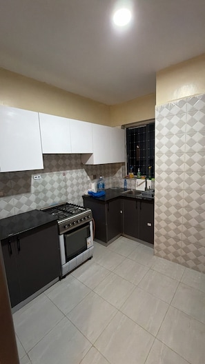 Cocina compacta con estufa a gas, horno y ventana con diseño de celosía.