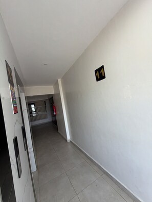 A corridor with a fire extinguisher, a door with a handle, and a wall with a number sign.