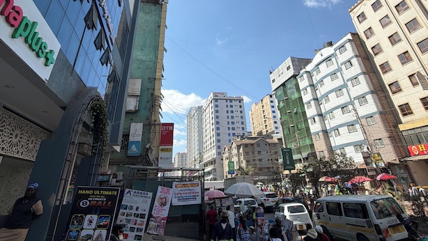 Una calle urbana concurrida con peatones, vehículos y edificios comerciales.