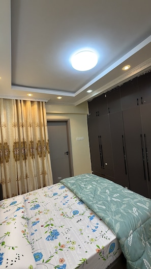 Un dormitorio con cama, cortinas, armario y lámpara de techo.