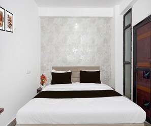 A bedroom with a bed, a nightstand, a vase with flowers, and a door with a window.