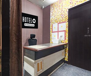 A hotel reception desk with a 'HOTELO' sign, a company-serviced label, a black chair, a white counter, and a tiled wall.