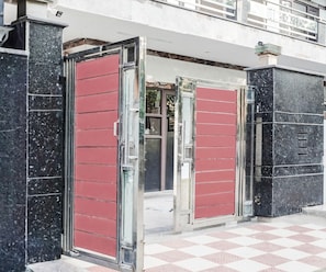 A building entrance with a checkered floor pattern, a metal gate, and a red door.