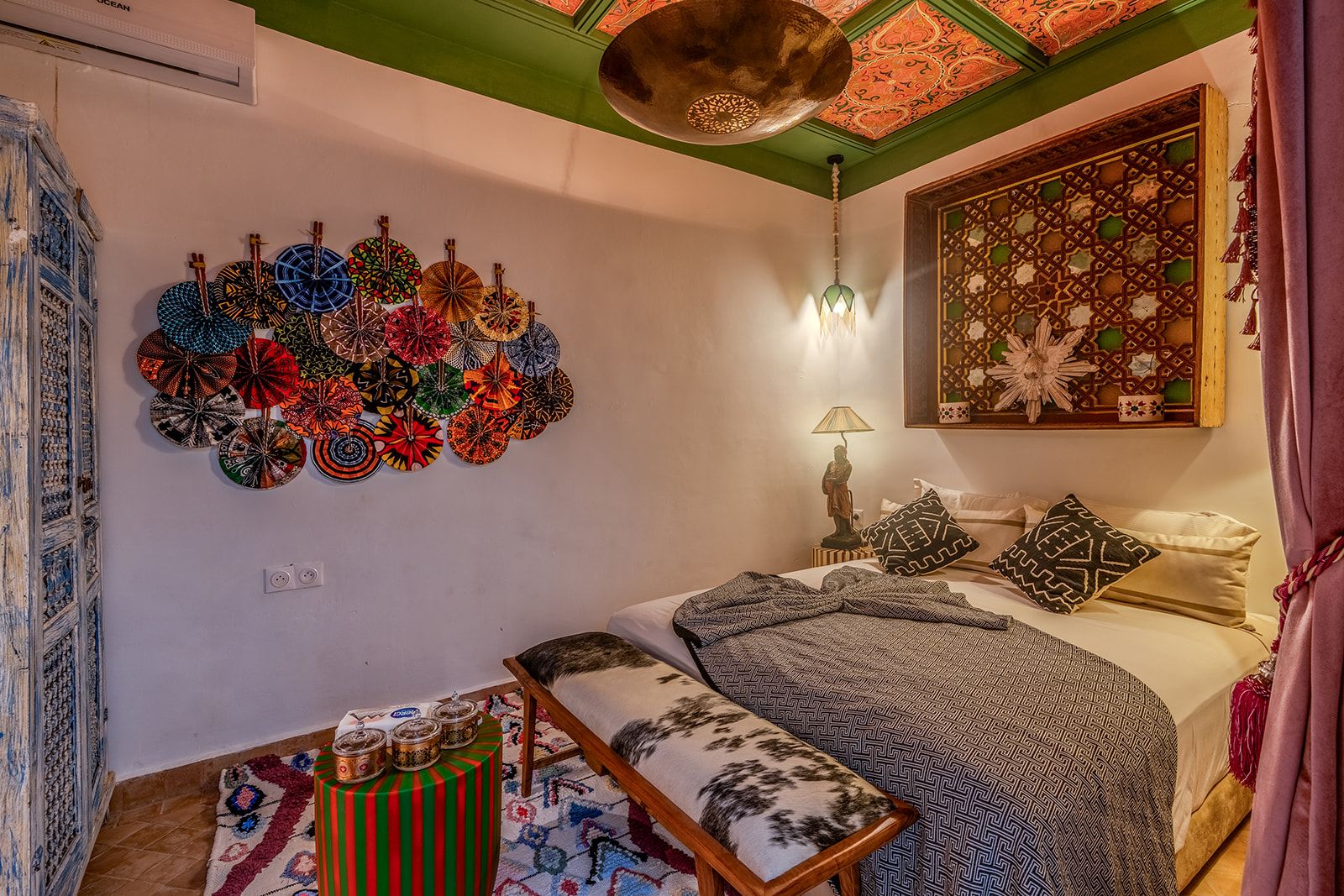 Una habitación con una cama, una pared decorada con platos coloridos, una lámpara y un biombo decorativo.