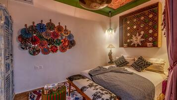 Una habitación con una cama, una pared decorada con platos coloridos, una lámpara y un biombo decorativo.