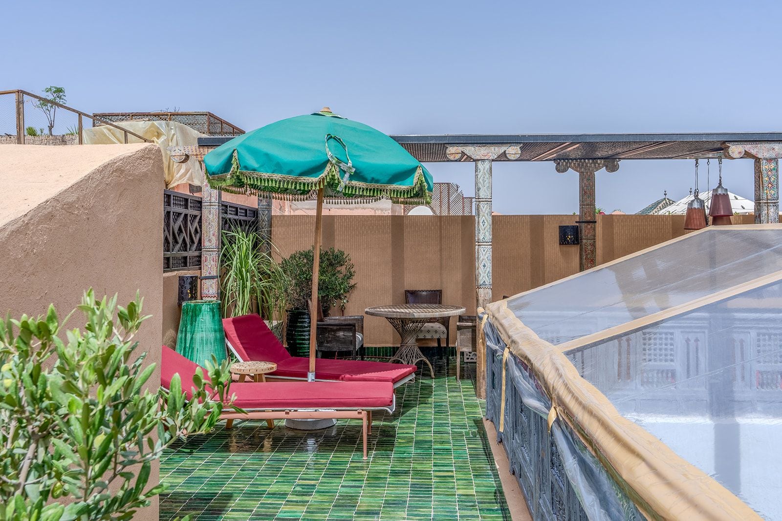 Una terraza en la azotea con piscina, sillas de descanso rojas y un paraguas verde.