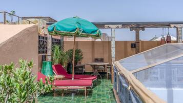 Una terraza en la azotea con piscina, sillas de descanso rojas y un paraguas verde.