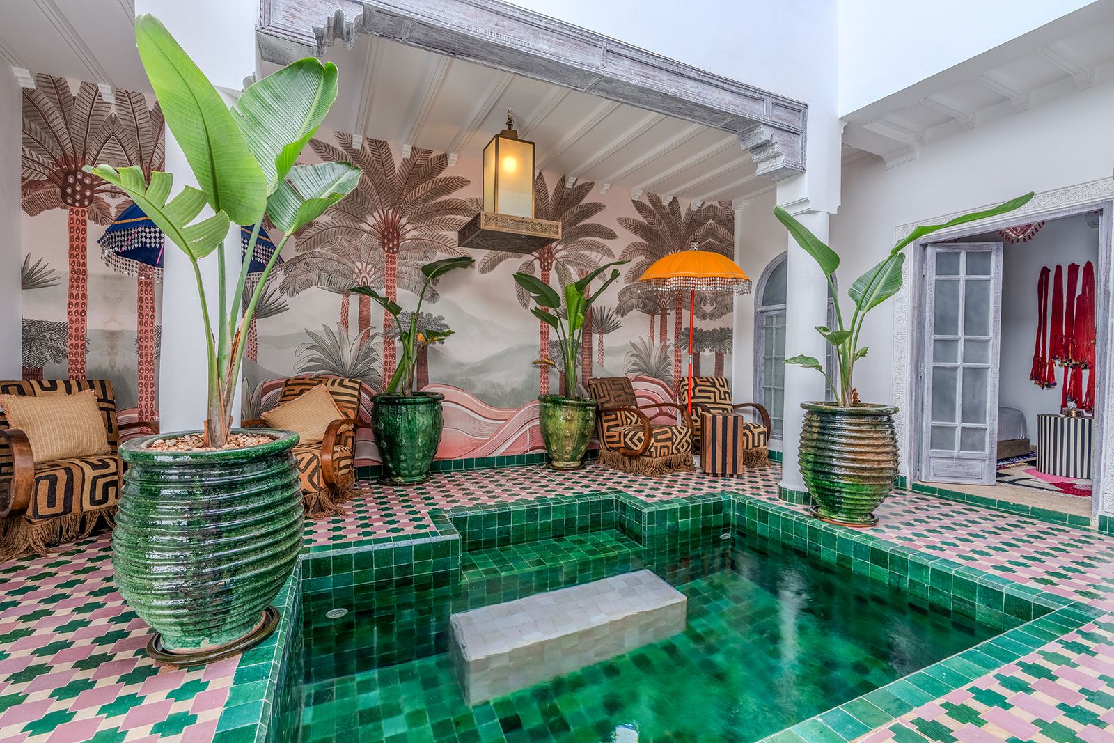 Un espace piscine doté d’un sol carrelé, de plantes en pot et d’un coin salon avec des coussins à motifs.