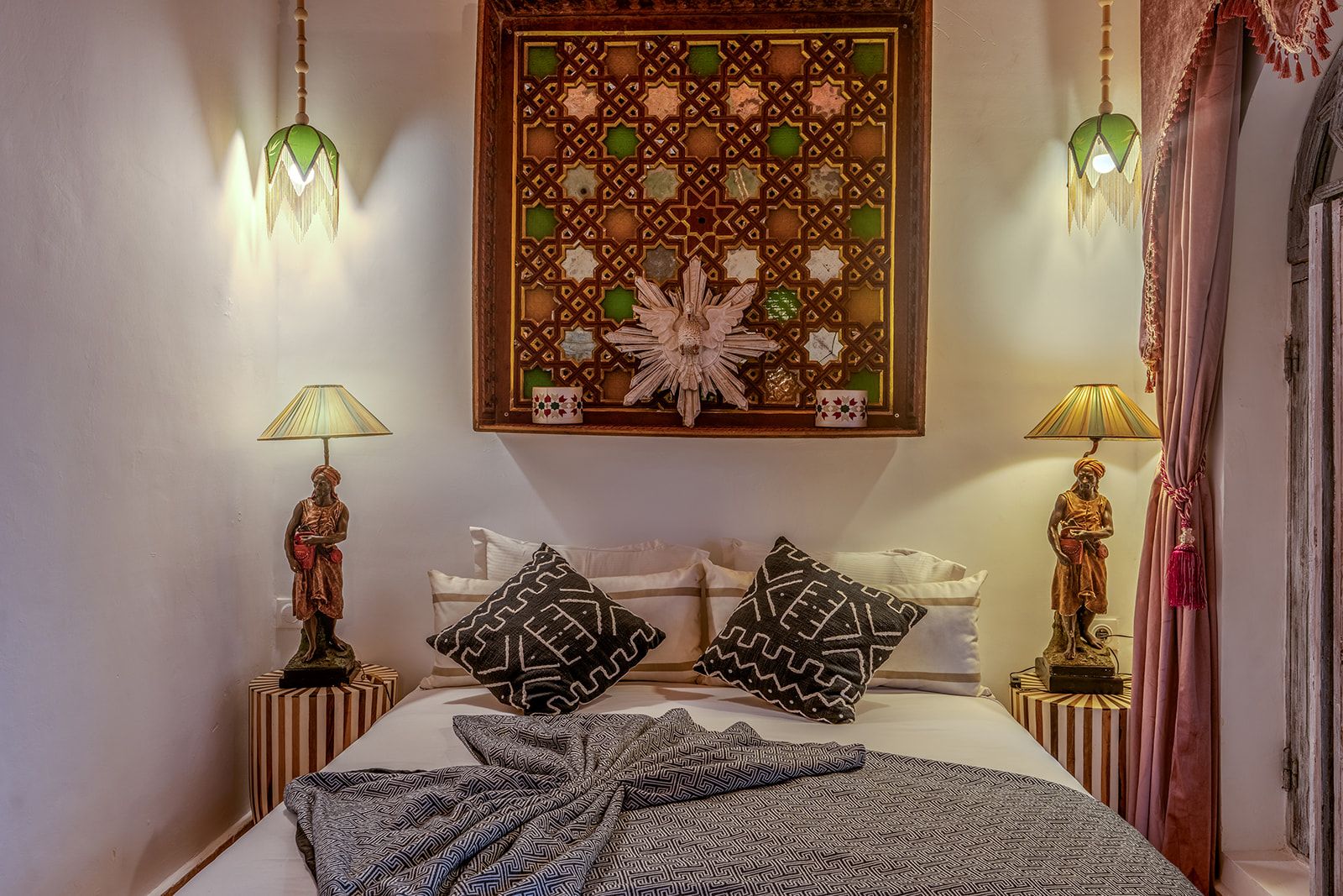 Ein Schlafzimmer mit einem Bett, Kissen mit Muster, zwei Nachttischlampen und einer Wanddekoration.