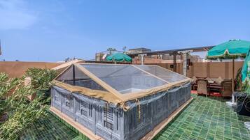 Una terraza en la azotea con zona cubierta, mobiliario exterior y vistas de los edificios circundantes.