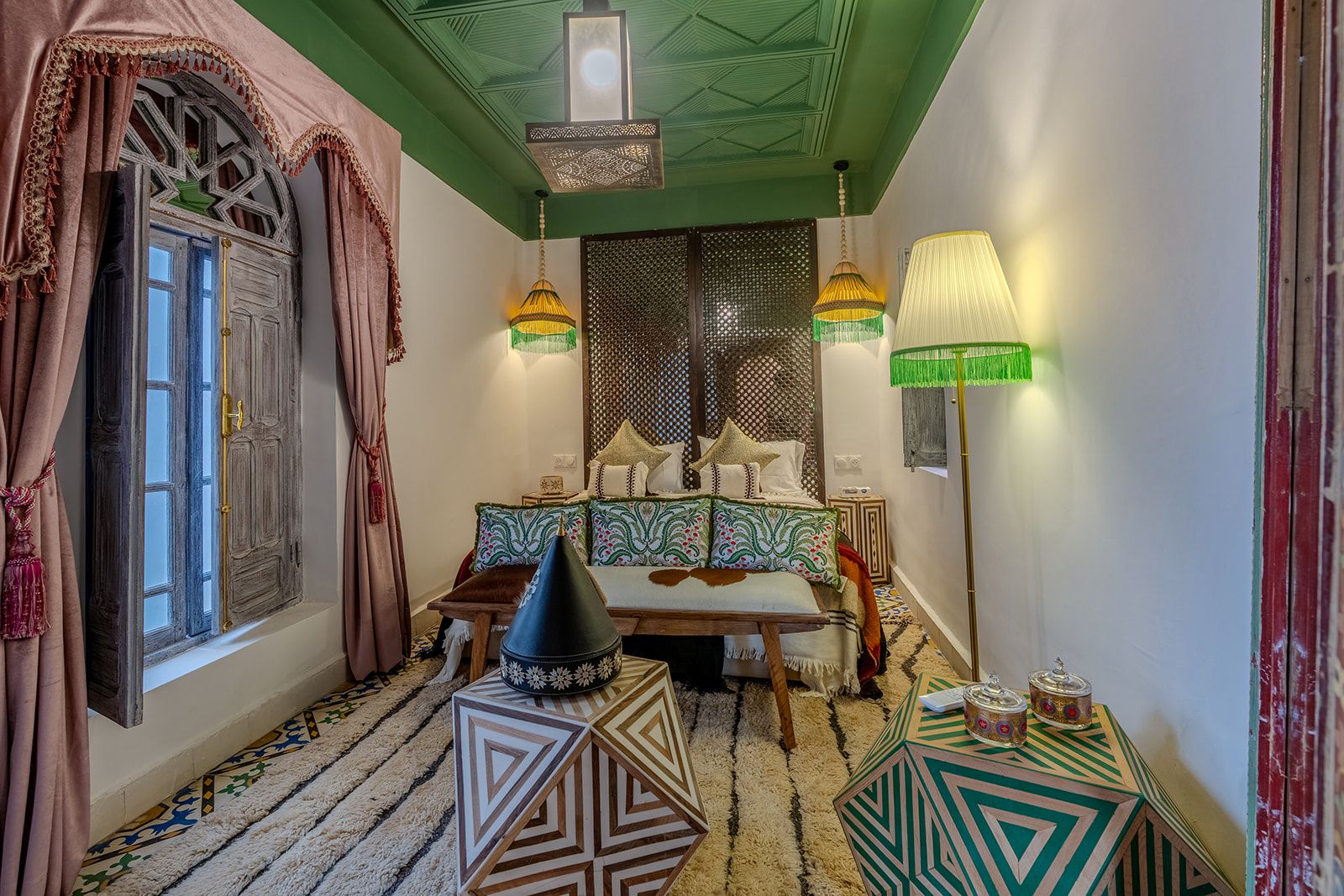 Een kamer met een bed, een hanglamp, een tafel met drankjes en een kamerbreed tapijt.