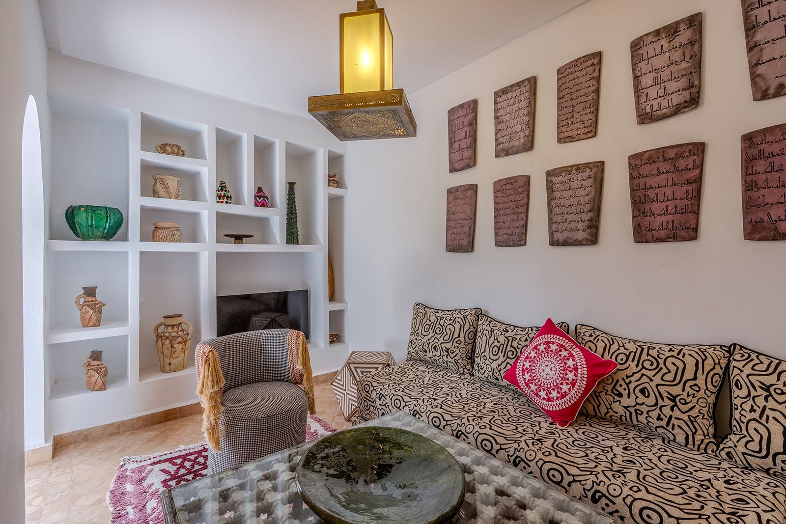 Un salon comprenant un canapé, un coussin décoratif à motifs, une table basse avec un bol décoratif, une cheminée et des étagères où sont disposés divers objets.