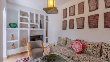 Un salon comprenant un canapé, un coussin décoratif à motifs, une table basse avec un bol décoratif, une cheminée et des étagères où sont disposés divers objets.