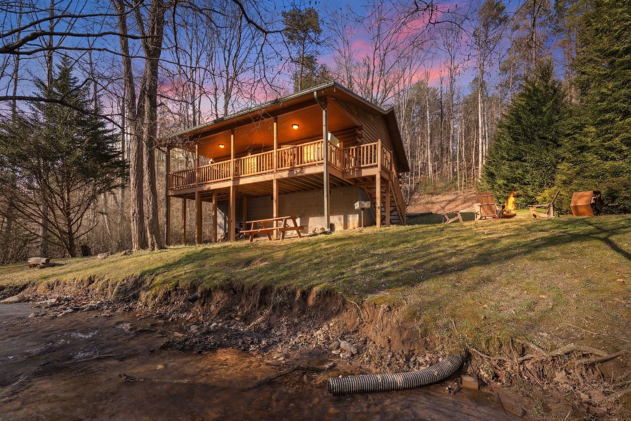 A cabin with a balcony, a picnic table, and a fire pit in a forest setting.