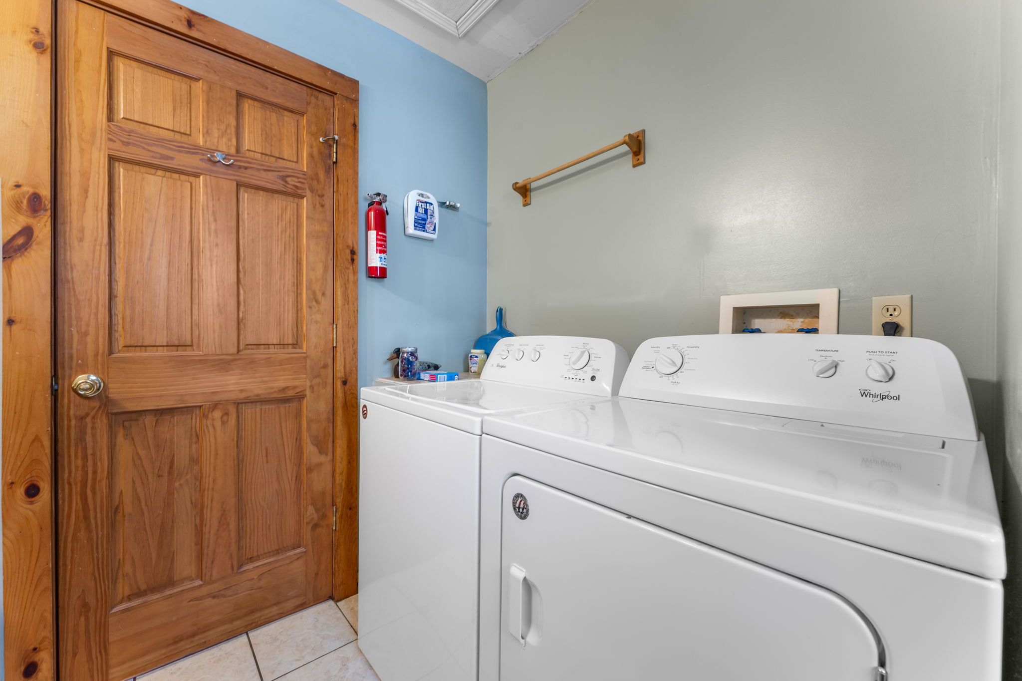 Een wasserette met een houten deur, een witte wasmachine, een droger en een blauwe muur.