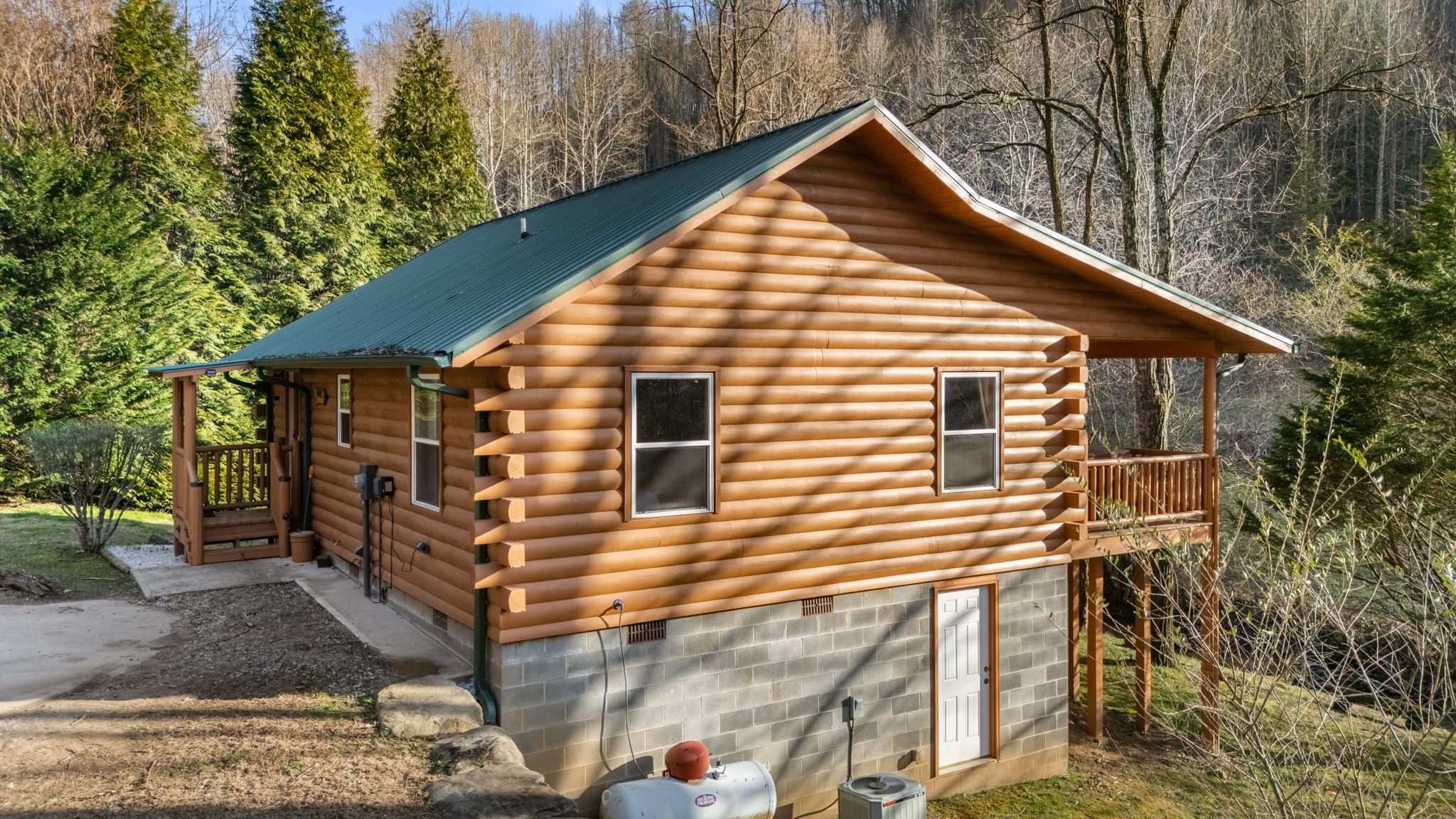Une cabane en rondins avec un porche, une cheminée et des fondations en pierre.