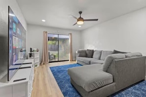 Un salon moderne avec un canapé d’angle gris, un téléviseur à écran plat et un ventilateur de plafond.